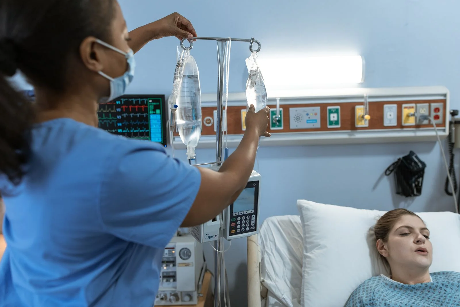 A nurse adjusting an IV beside a patient in a hospital bed; illustrative care-setting photograph